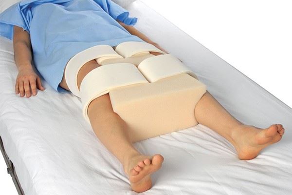 patient lying in bed with abduction wedge between legs