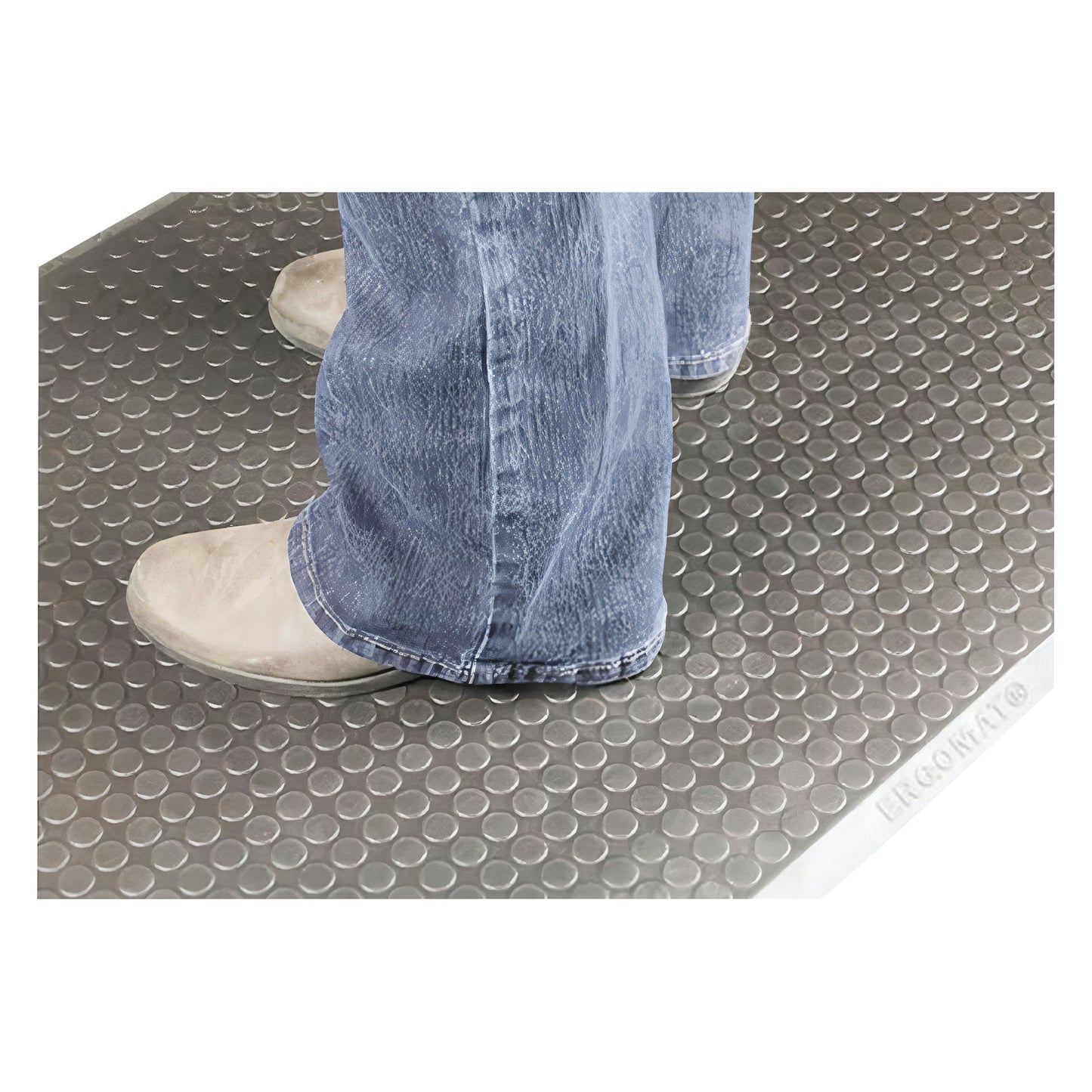 A person wearing jeans and beige shoes stands on the ERGOMAT Basic Smooth Anti-Fatigue Mat with a textured circular pattern.