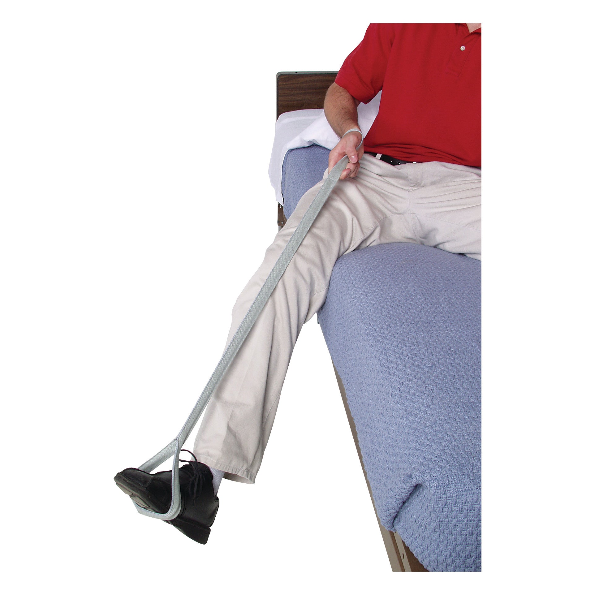 A person in beige pants and black shoes uses an AliMed Leg Lifter, a long assistive strap, to elevate their leg on a bed.