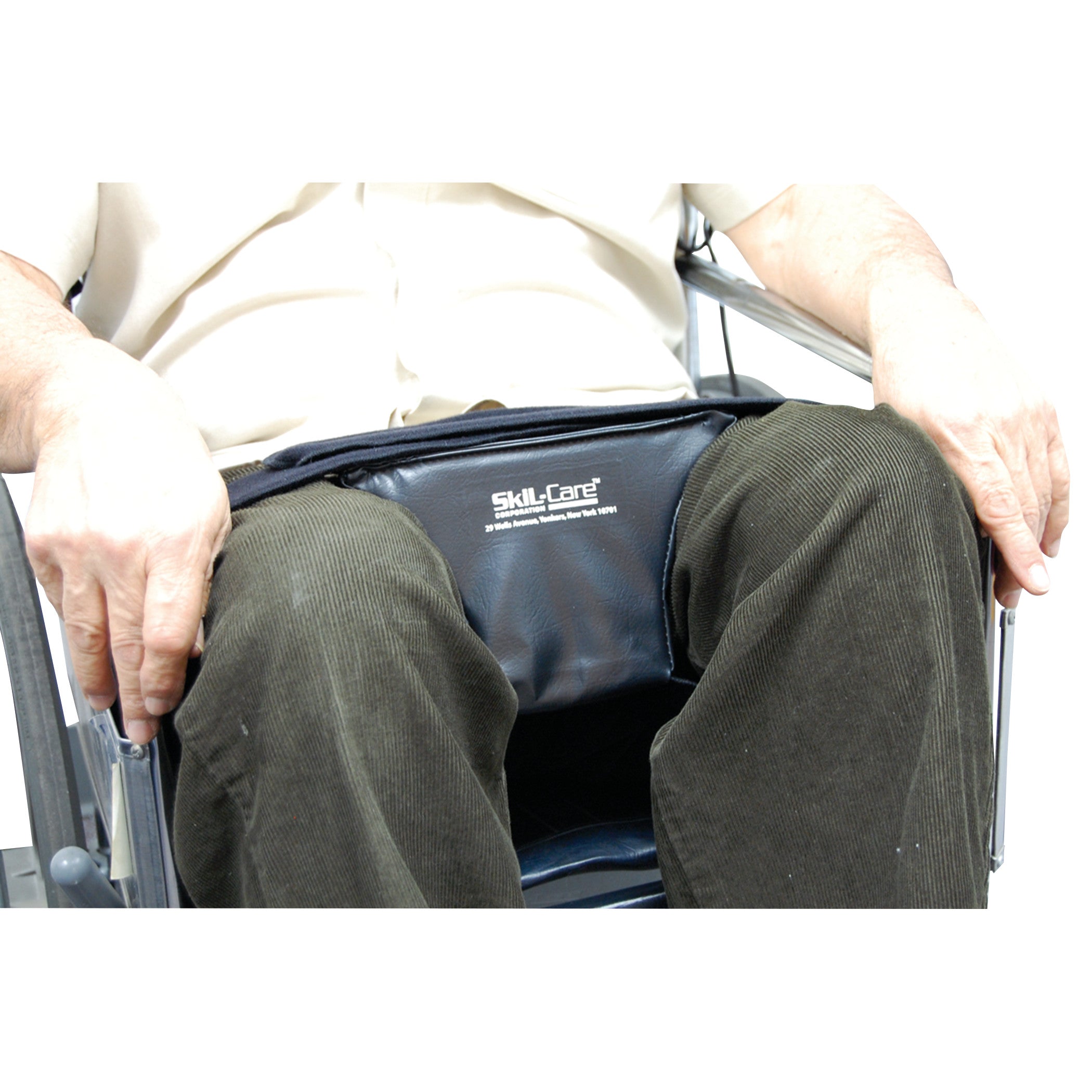 A person in a wheelchair uses the SkiL-Care Abduction Wedge, placed between the knees for support and alignment.