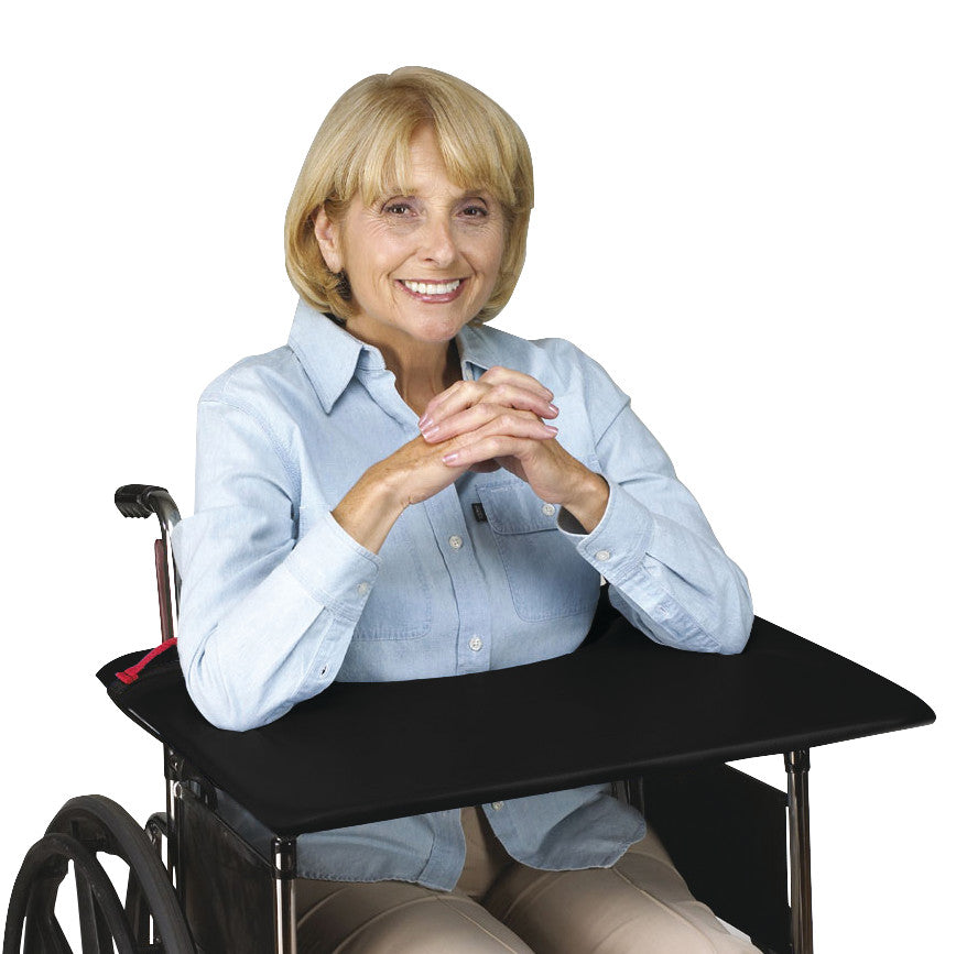An older adult smiles while seated in a wheelchair using a SkiL-Care Removable Wheelchair Lap Tray, with hands clasped on it.