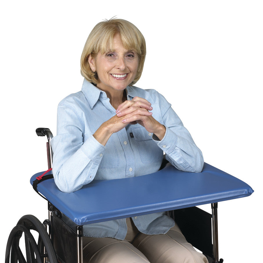 A person sits in a wheelchair using the SkiL-Care SofTop Lap Tray, which is blue and cushioned for comfort.