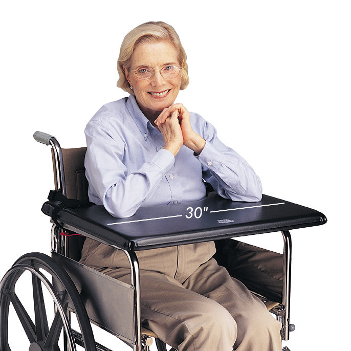 A person sits in a wheelchair using the SkiL-Care SofTop Lap Tray, measuring 30 inches wide, with a cushioned surface.