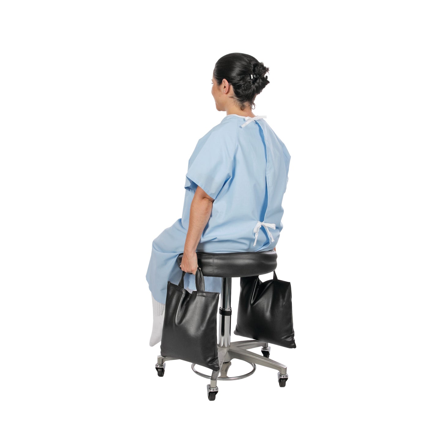 A person sits on a stool in a medical gown holding AliMed Cervical Visualization and Traction Sandbags, one in each hand.