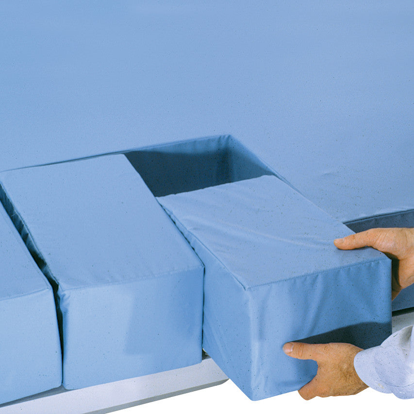A person adjusts a section of the AliMed Echostretcher Pad, featuring removable blue padded blocks on a medical examination table.