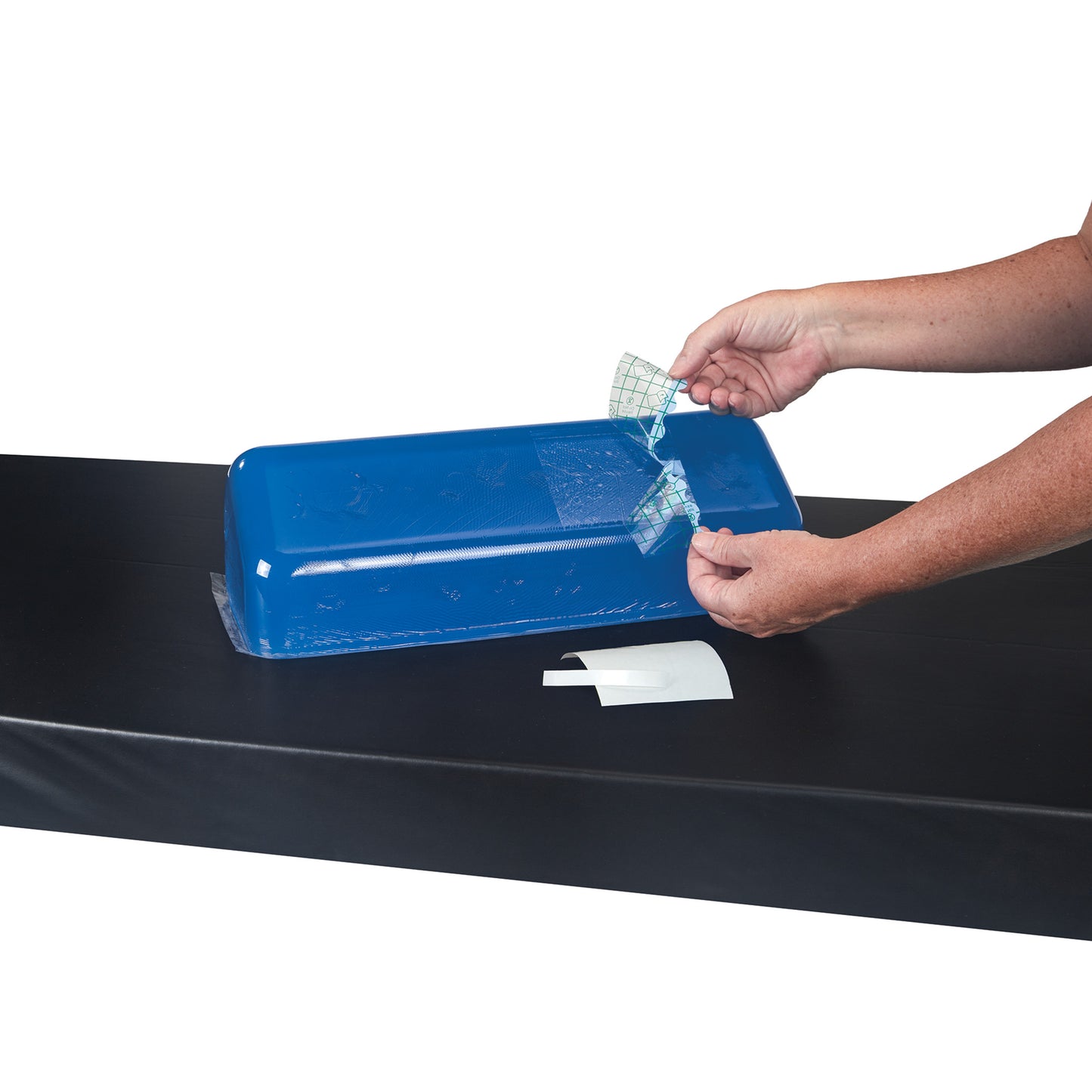 A person uses the AliMed Gel Repair Kit to apply a patch to a blue gel cushion on a black surface.