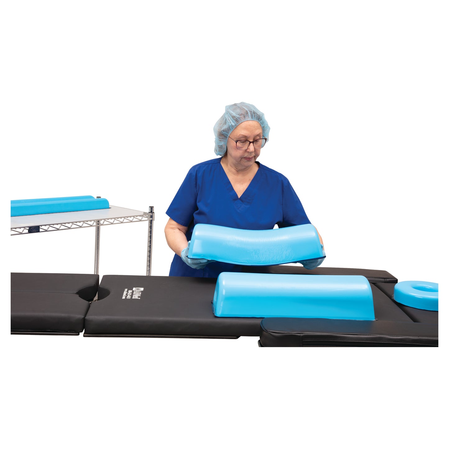 A person arranges an AliMed AliBlue Lite Hybrid Gel Chest Roll on a padded black surface, wearing blue scrubs and a hair cover.