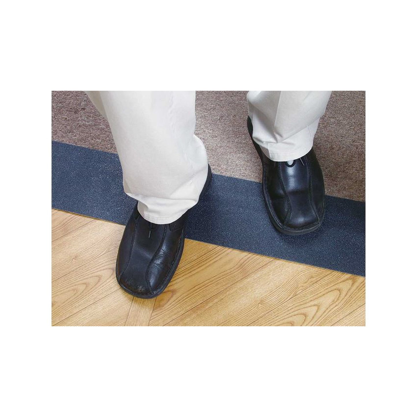 A person wearing cream-colored pants and black shoes stands with feet on Anti-Slip Adhesive Tape on a wood and carpet floor.