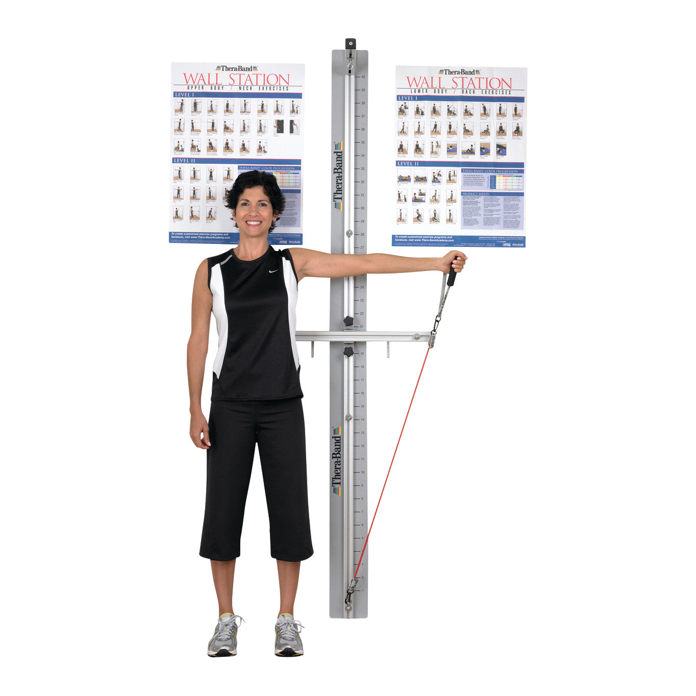 A woman exercises using a THERABAND Wall Station, holding a handle attached to a resistance band with exercise charts in the background.