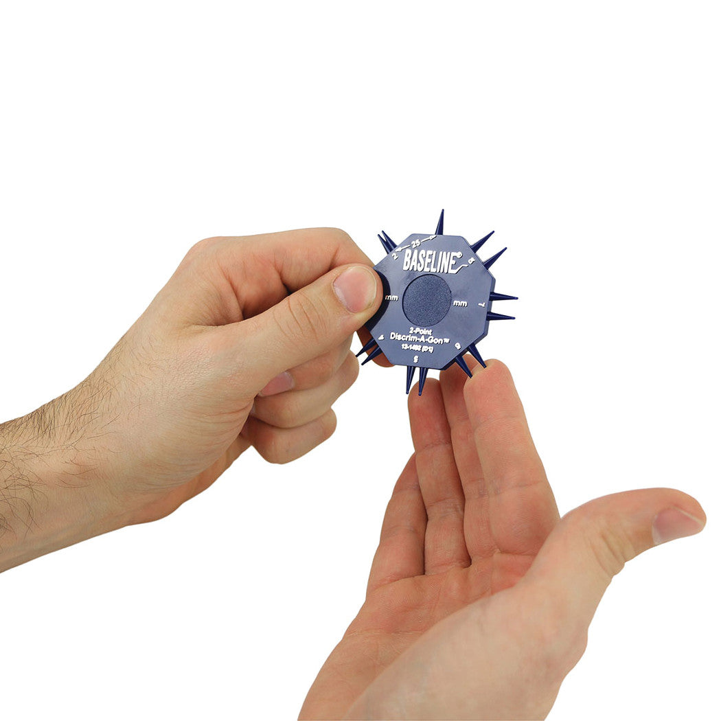 A person holds a Baseline DISCRIM-A-GON, a blue plastic tool with spikes around its edge, used for sensory evaluation.