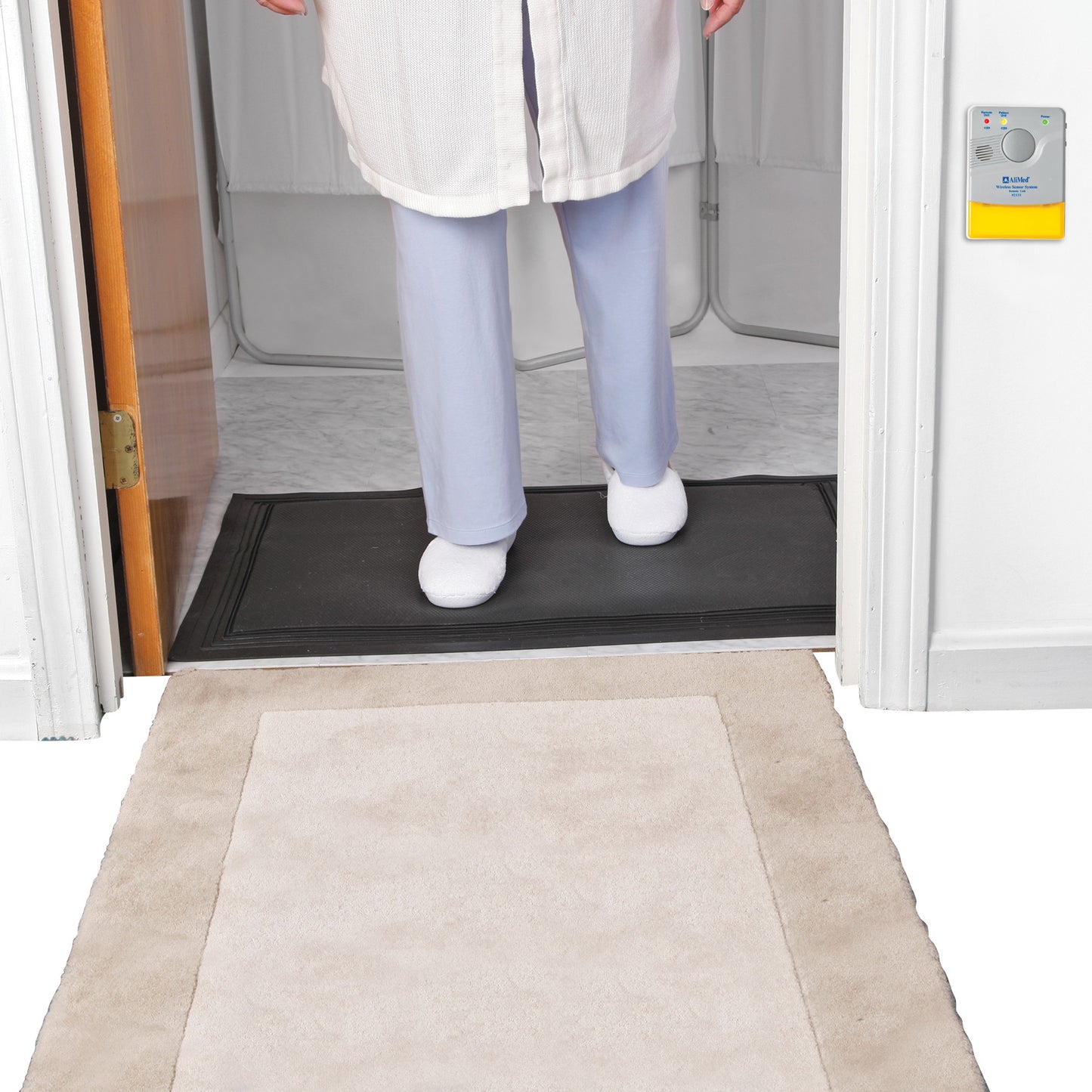 A person stands on an AliMed Nonslip Exit Alarm Mat by a doorway. A security device is mounted on the wall nearby.