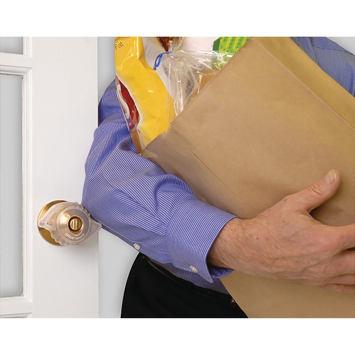 A person uses an elbow to open a door with a rounded knob covered by a Great Grips handle, while carrying a brown grocery bag.