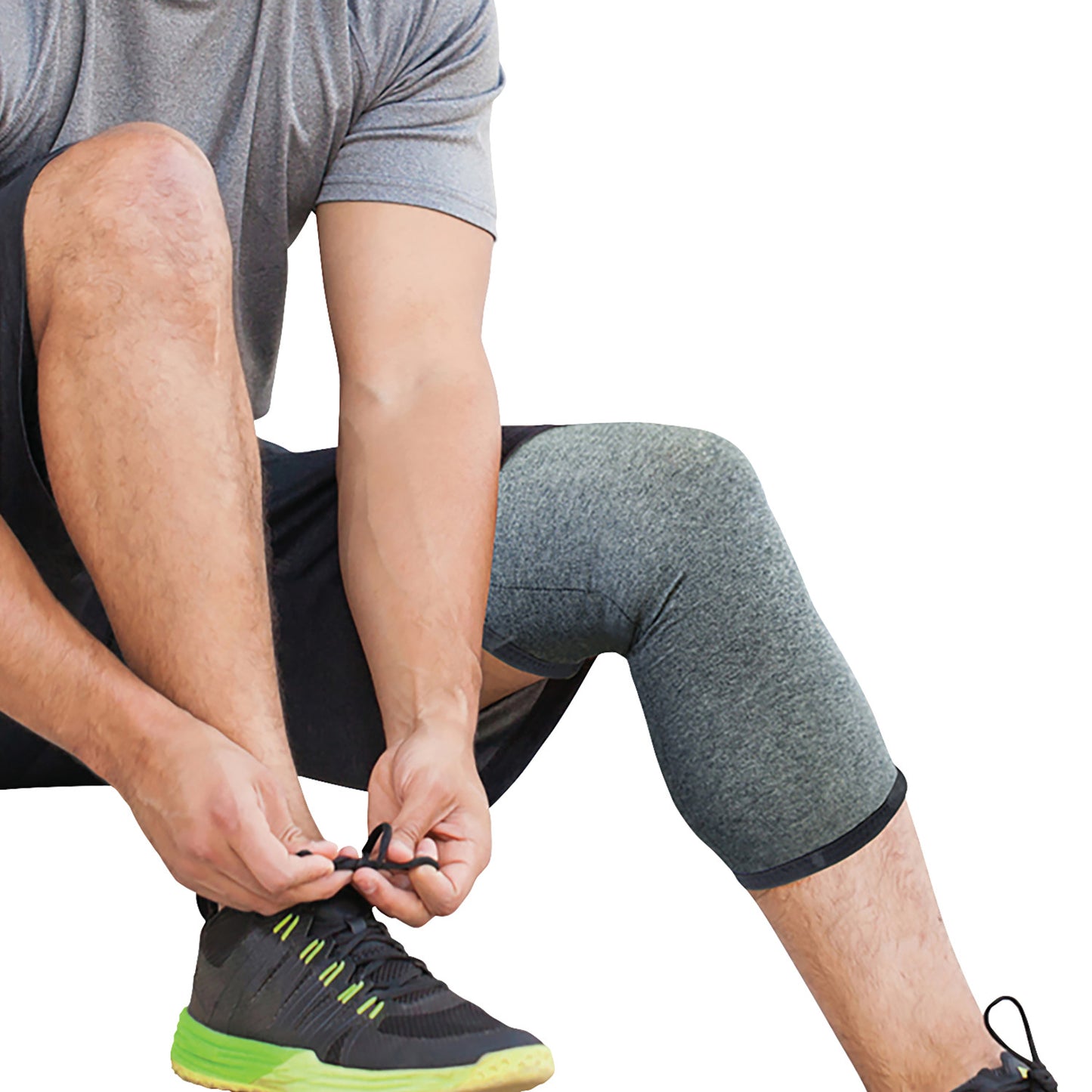 A person wears a Brownmed IMAK Compression Arthritis Knee Sleeve while tying their sporty black and lime green shoes.