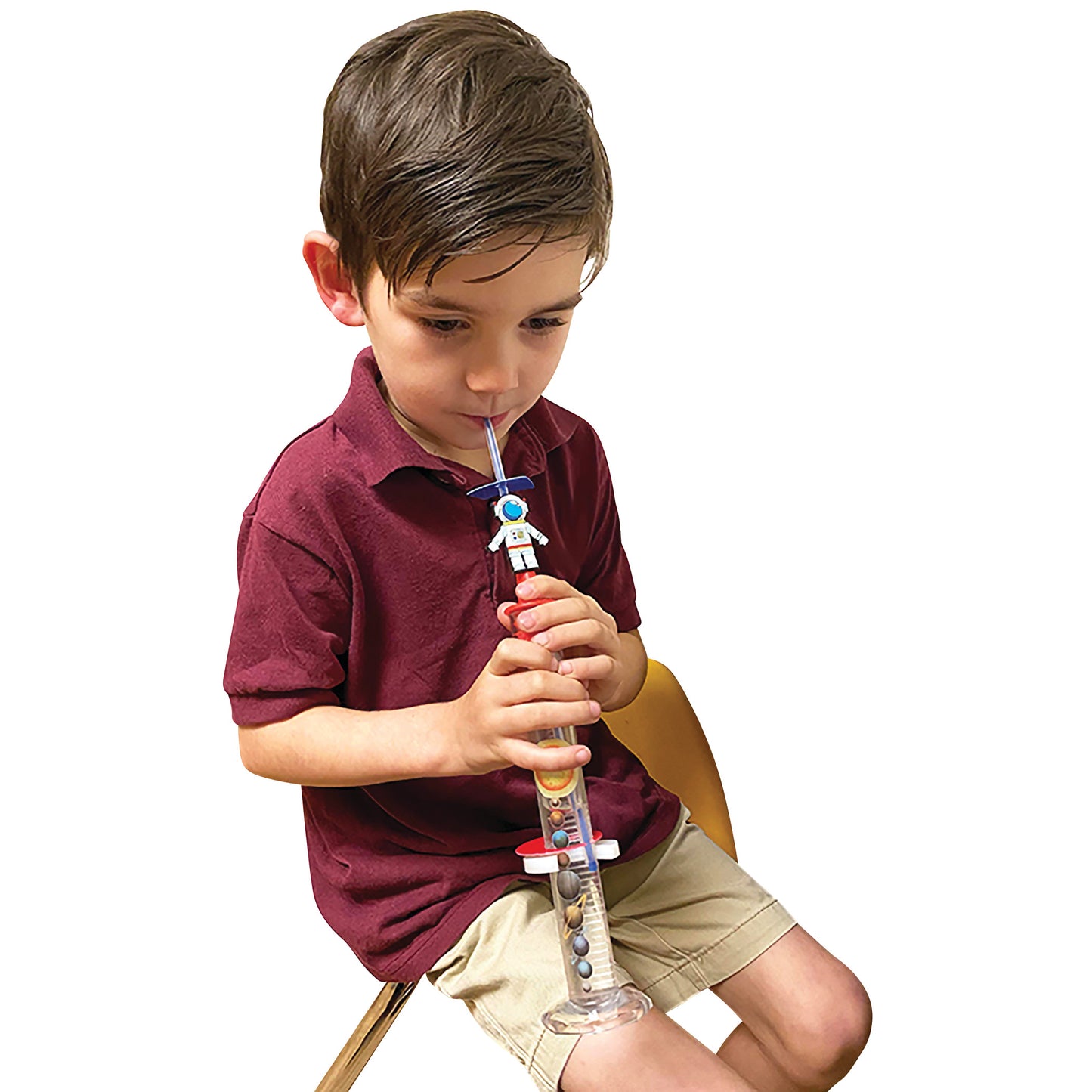 A child uses the TheraSIP RocketSIP, a tube toy with a rocket design, while seated in a chair, wearing a maroon shirt and shorts.