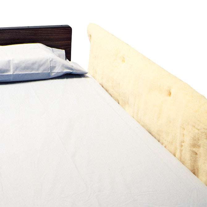 A SkiL-Care Synthetic Sheepskin Bed Rail Pad is attached to a bed rail, next to a pillow and bedsheet.