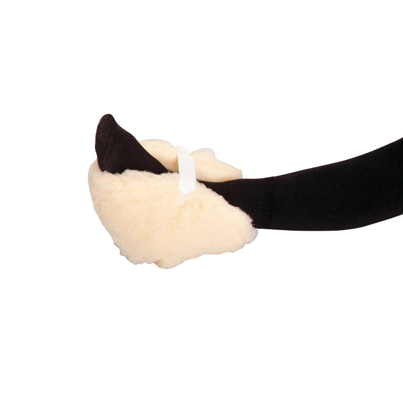 A foot wearing a SkiL-Care Stay-On Heel Protector. It's a soft, beige cushion with a black sock and a white strap securing it.