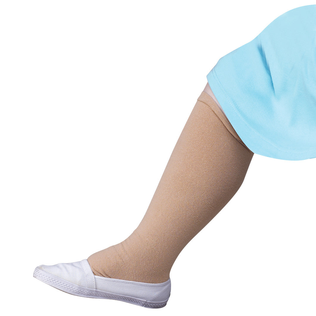 A leg in a beige SkiL-Care Geri-Sleeve, wearing a white shoe and blue garment, against a plain background.