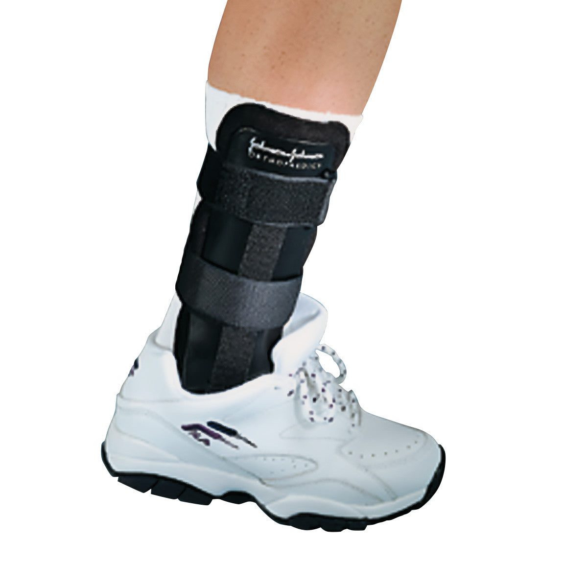 A leg wearing a FLOAM Ankle Stirrup Brace inside a white sneaker, providing support with adjustable black straps.