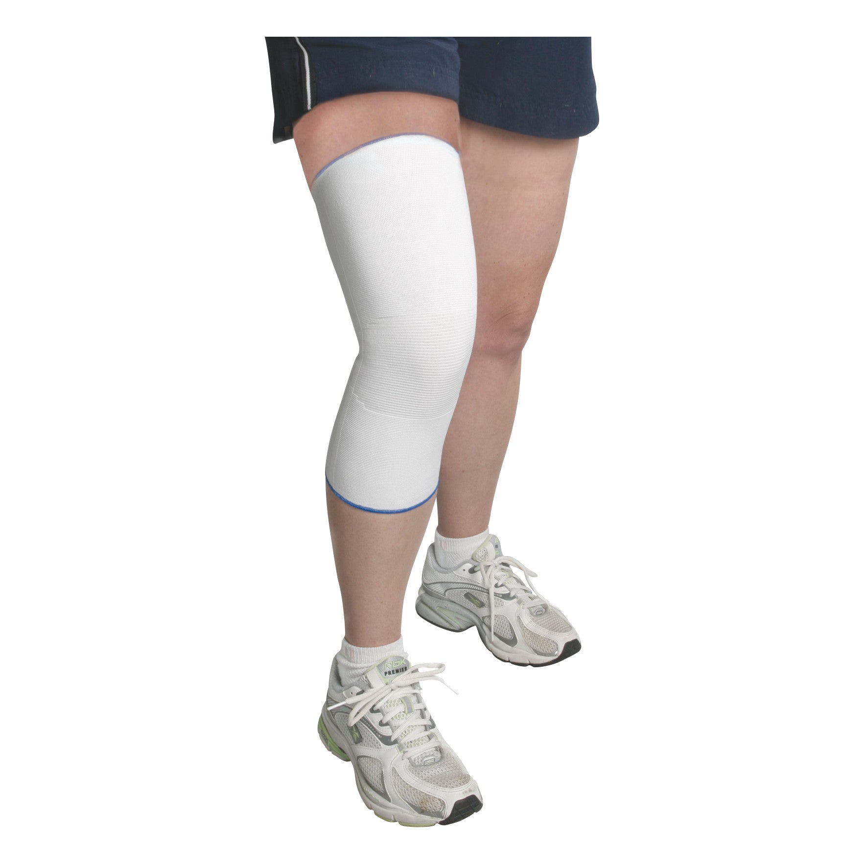 A person wears an AliMed Seamless Knee Sleeve on their right leg. They are dressed in shorts and sneakers.