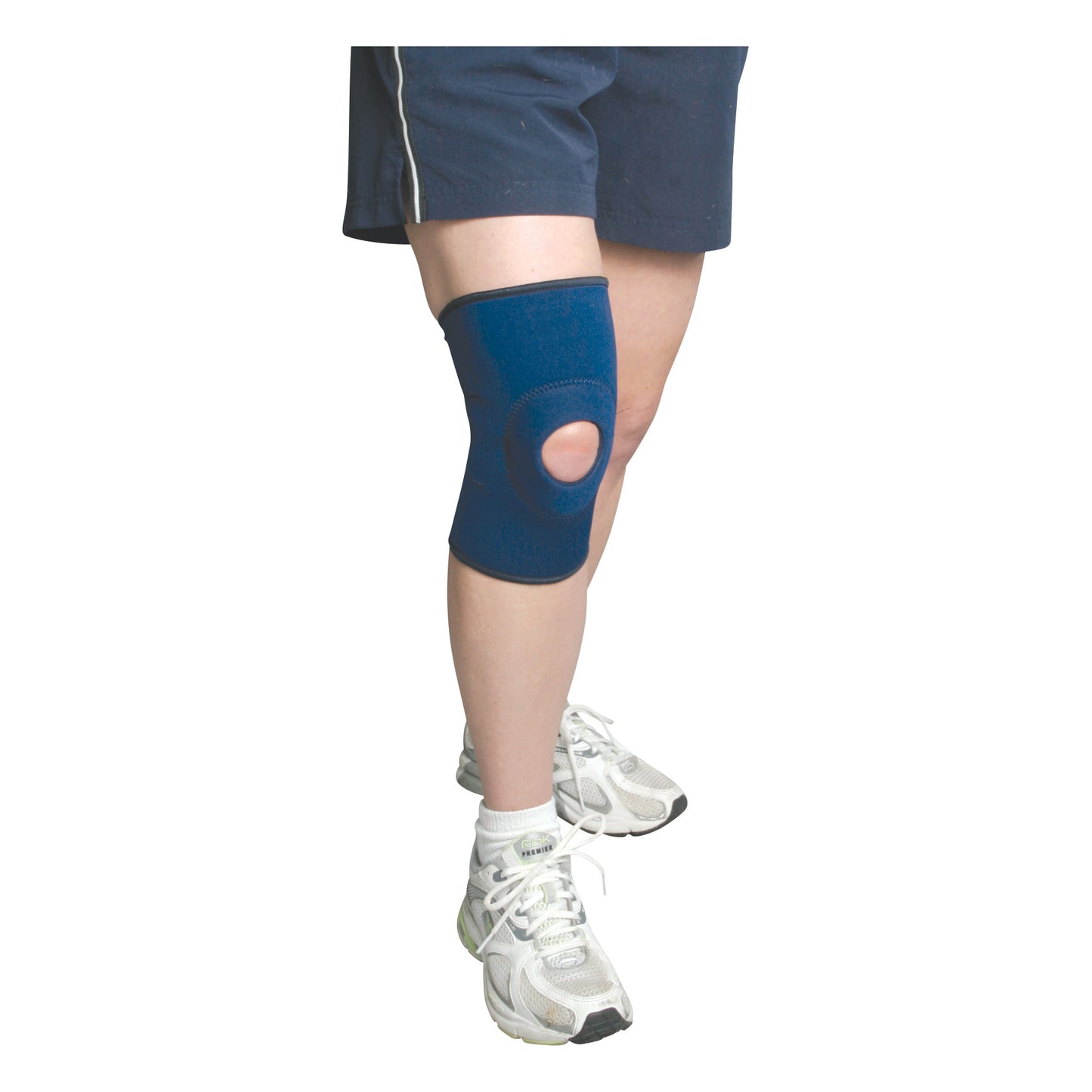 Person wearing the AliMed Knee Support with Open Patella, navy blue, over bare knee. They are also wearing shorts and sneakers.