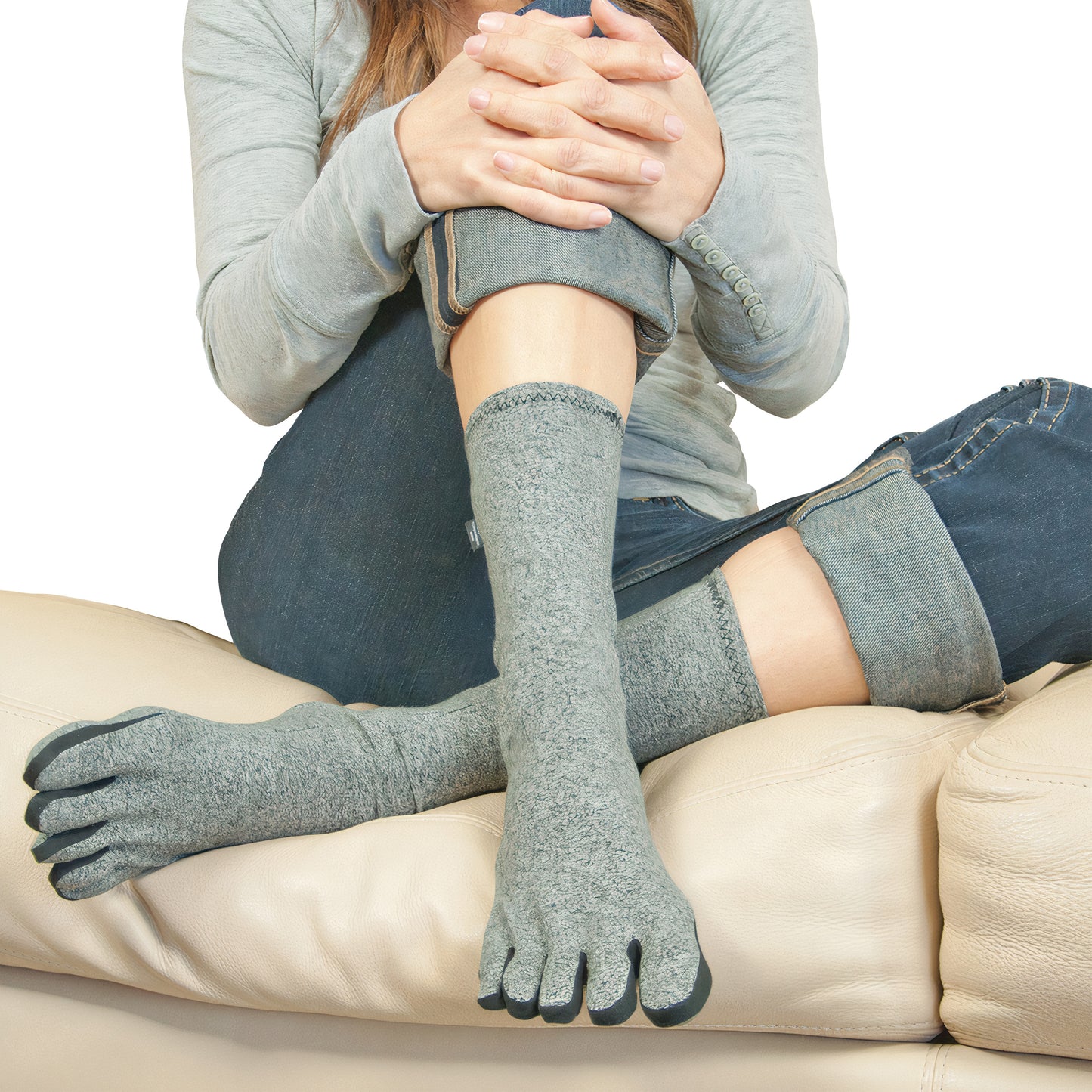 A person wearing Brownmed IMAK Compression Arthritis Socks, gray toe socks, sitting with legs crossed on a beige couch.