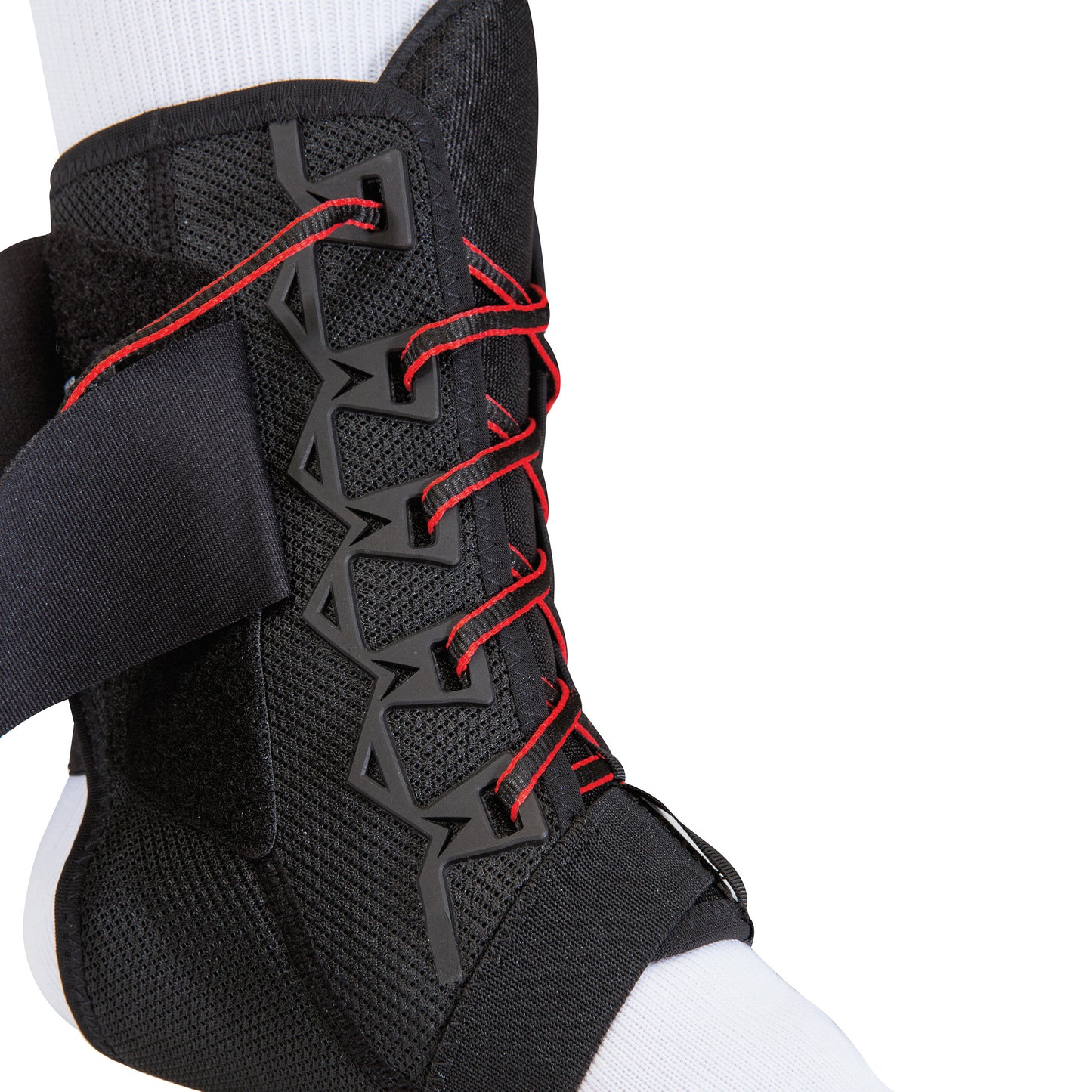 A Mueller The One Ankle Brace, black with red laces and strap, is worn over a white sock, providing support and stability.