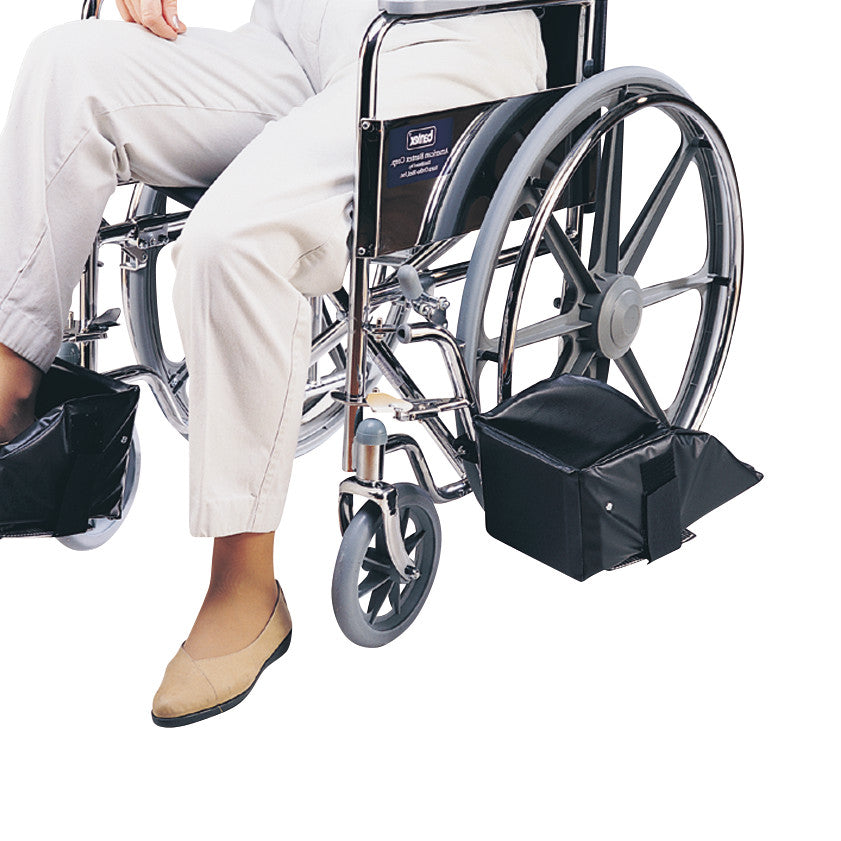 Person seated in a wheelchair using SkiL-Care Swing-Away Foot Support, featuring cushioned footrests and a sturdy metal frame.