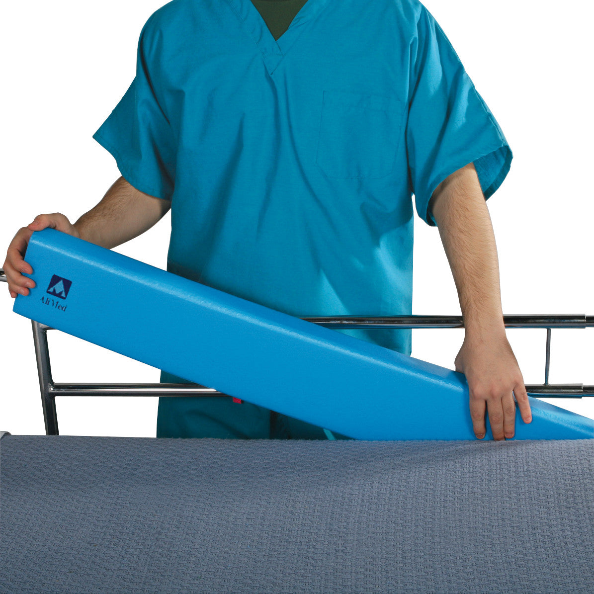 A person places the AliMed Antimicrobial Bed Stuffer Safety Bolster, a blue foam wedge, on a bed with a gray cover.