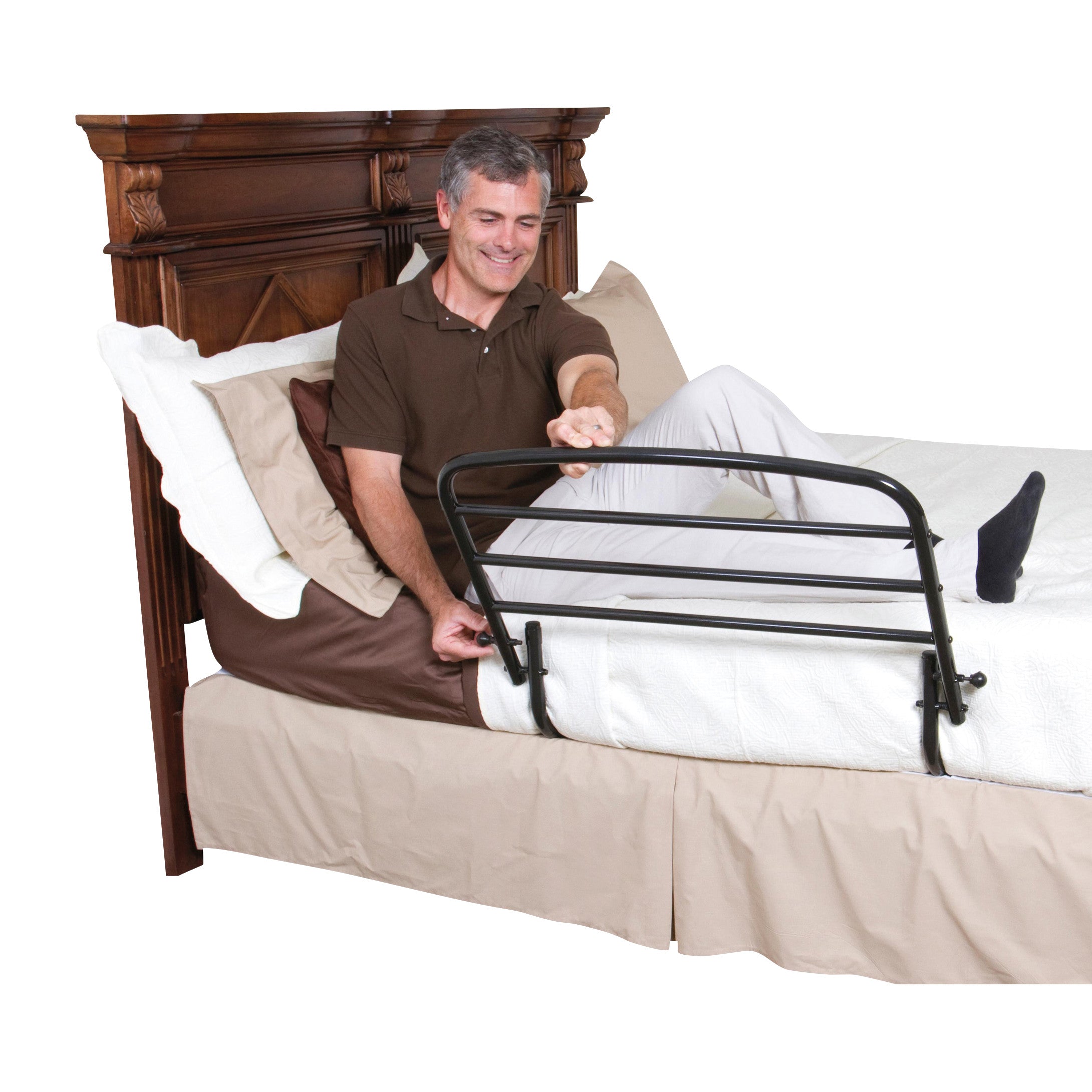 A person uses the Stander 30' Safety Bed Rail attached to a bed with a wooden headboard. The rail is black and foldable.