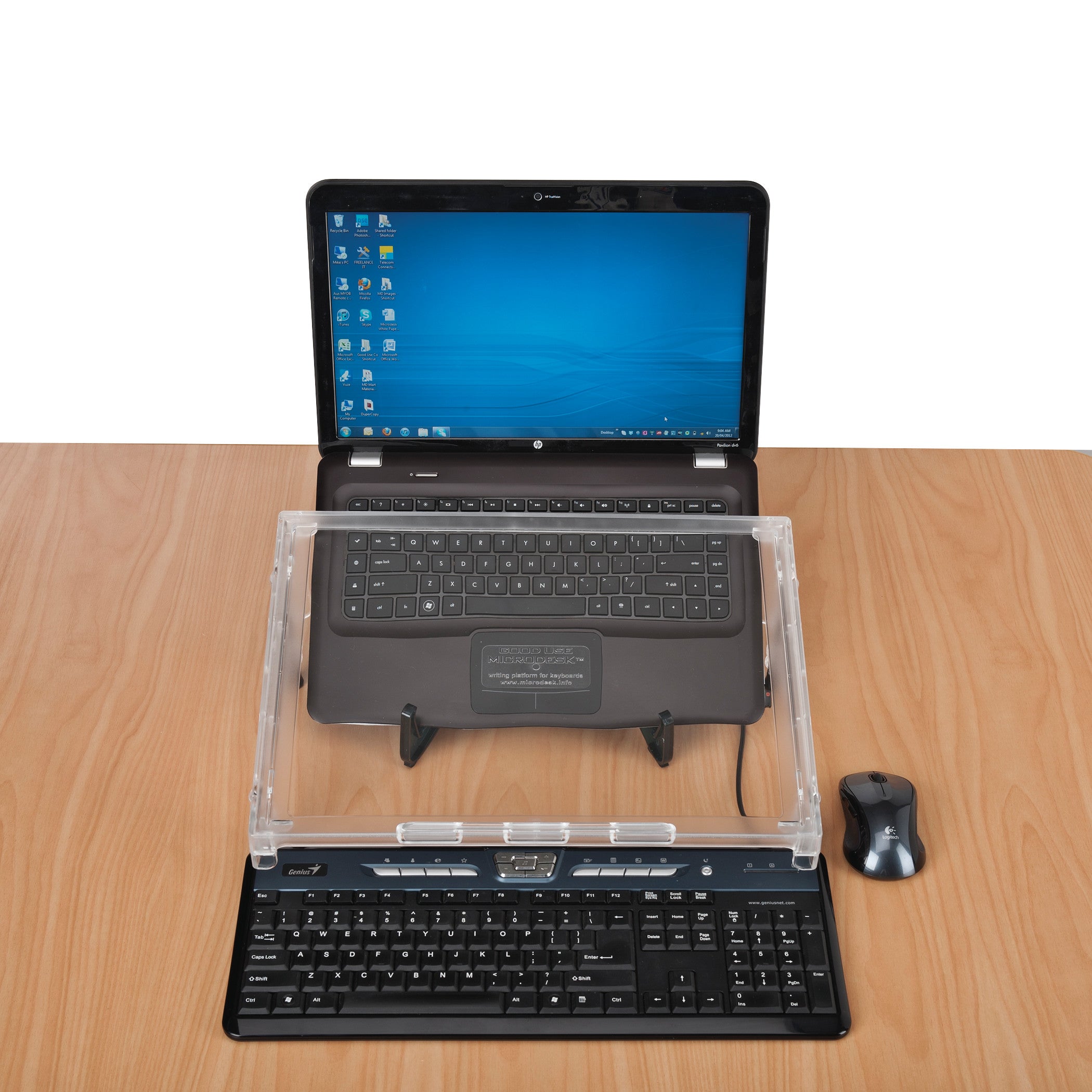 A Microdesk Compact Writing Platform sits on a wooden desk between a laptop and a keyboard, with a mouse beside it.