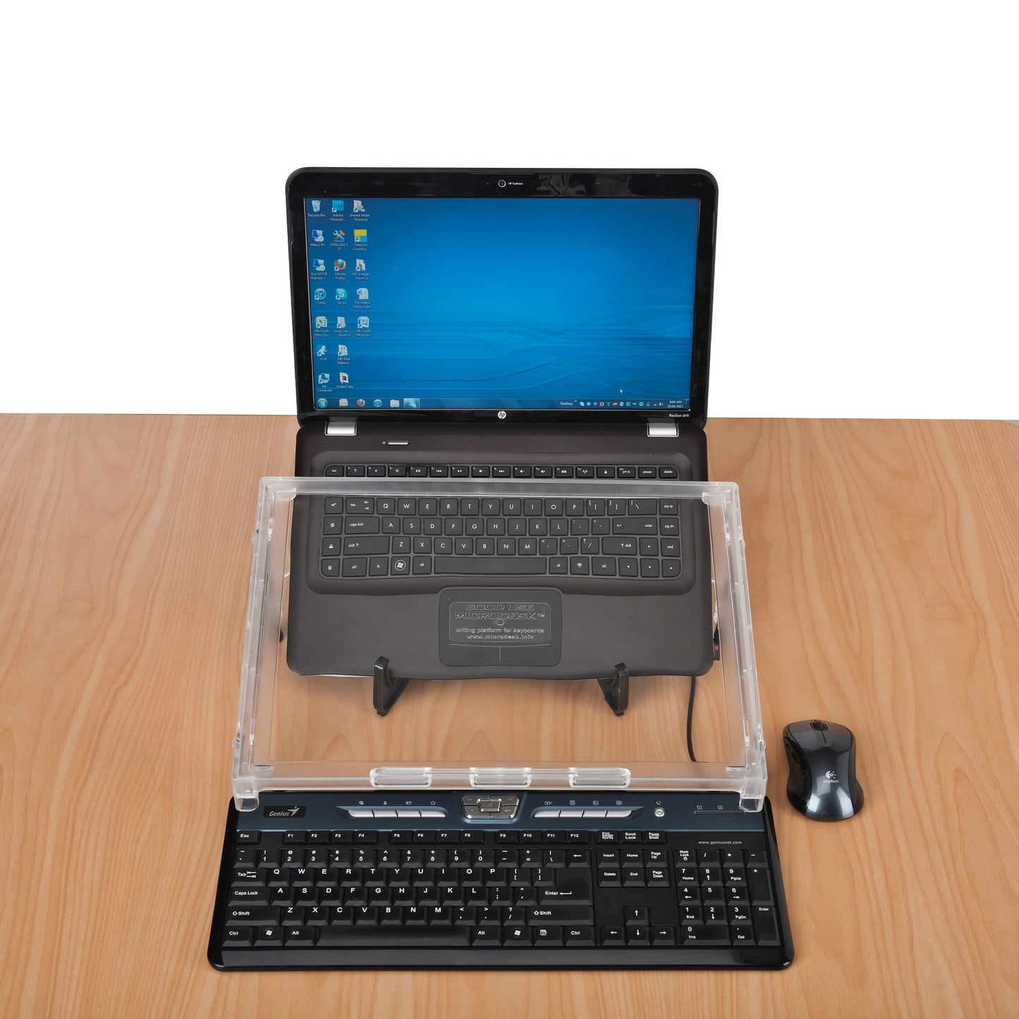A Microdesk Compact Writing Platform sits on a wooden desk between a laptop and a keyboard, with a mouse beside it.