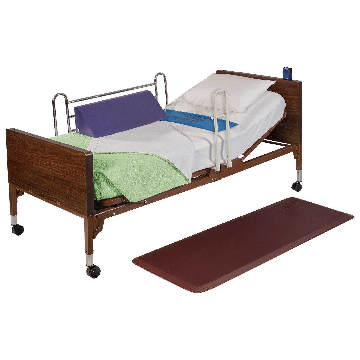 A Drive Medical PrimeMat positioned beside a hospital bed with side rails, pillows, and a green blanket draped over.
