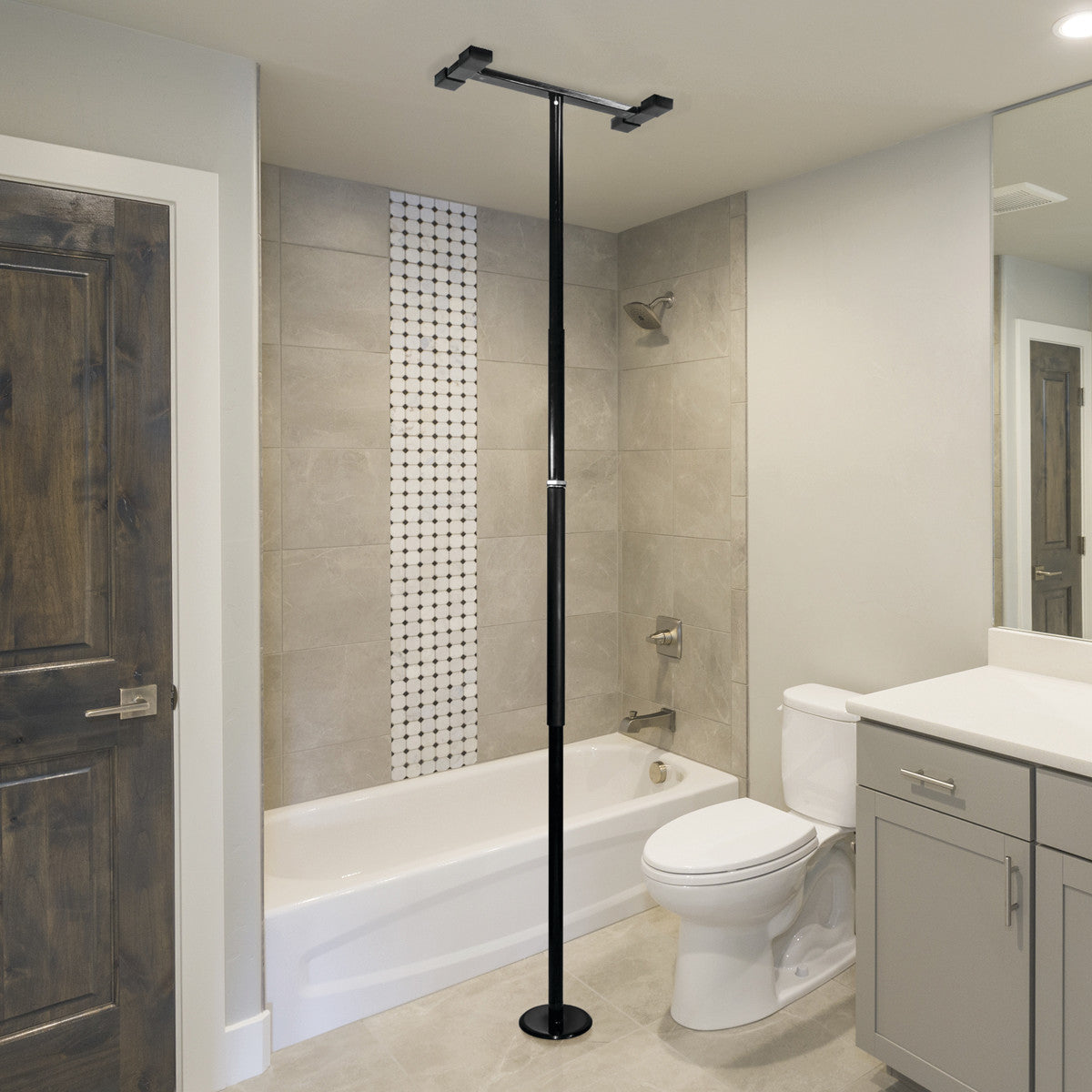 A Security Pole installed between the floor and ceiling in a bathroom beside a bathtub and toilet, with beige tiles and a vanity.
