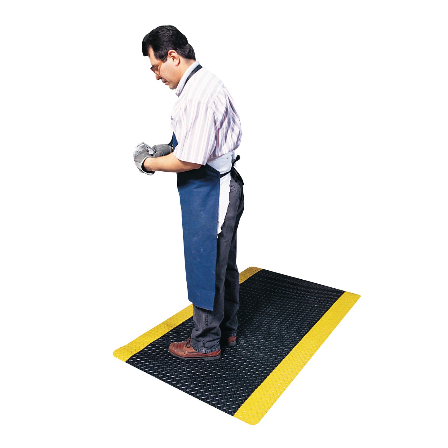 A man wearing an apron and gloves stands on a black Saddle Trax Anti-Fatigue Mat with yellow edges, providing ergonomic support.