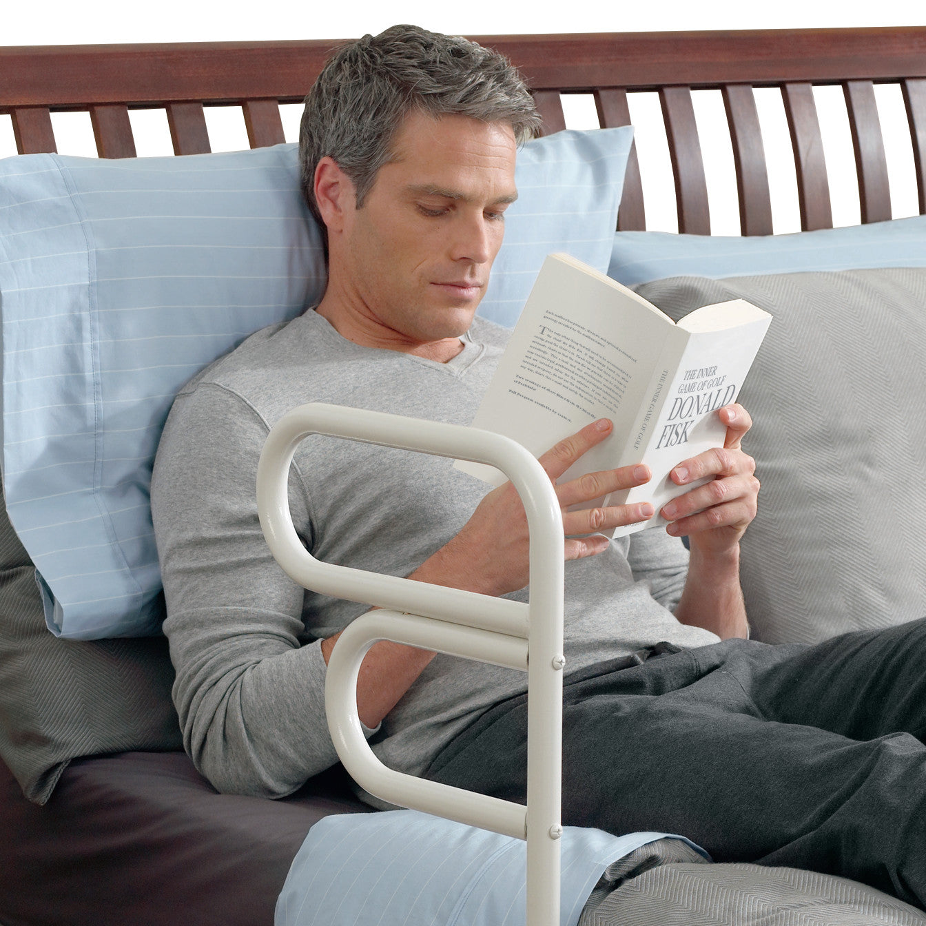 A person is reading in bed, supported by the Arcorail Bed Rail, featuring a sturdy, ergonomic design for easy access and safety.