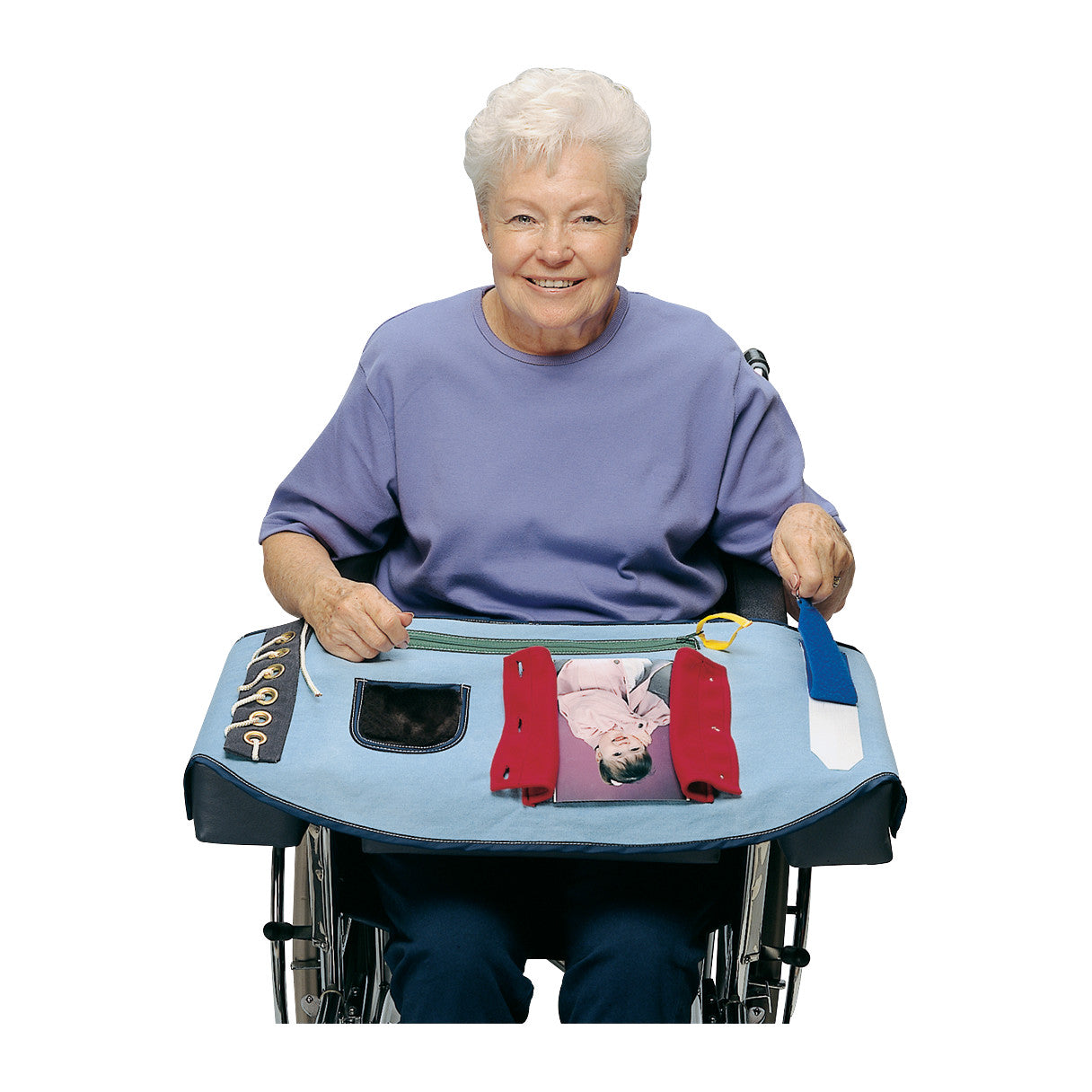 An elderly woman in a wheelchair uses the Posey Happy Hands Overlay, a blue activity mat with laces, zippers, and pockets.