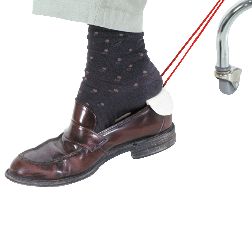 A foot with a dark sock in a brown loafer, using the AliMed Shoe Aid for pulling on shoes, attached to a metal frame.