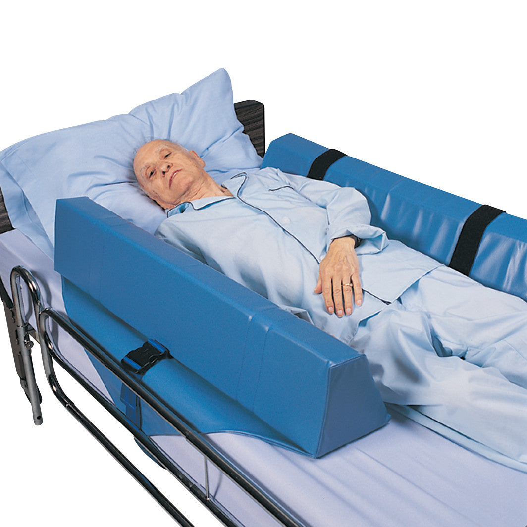 An elderly person lies in bed using the SkiL-Care Roll-Control Bed Bolster, featuring blue padded guards on both sides for safety.
