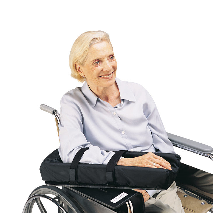 An older adult in a wheelchair uses the SkiL-Care Level Wheelchair Mobile Arm Support, a padded black sling for arm comfort.