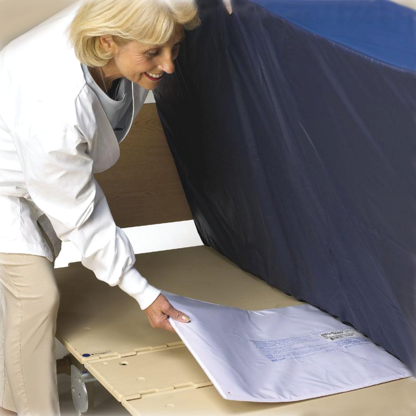 A person is setting up the SkiL-Care BedPro UnderMattress Alarm System with a mat placed under a mattress for monitoring.