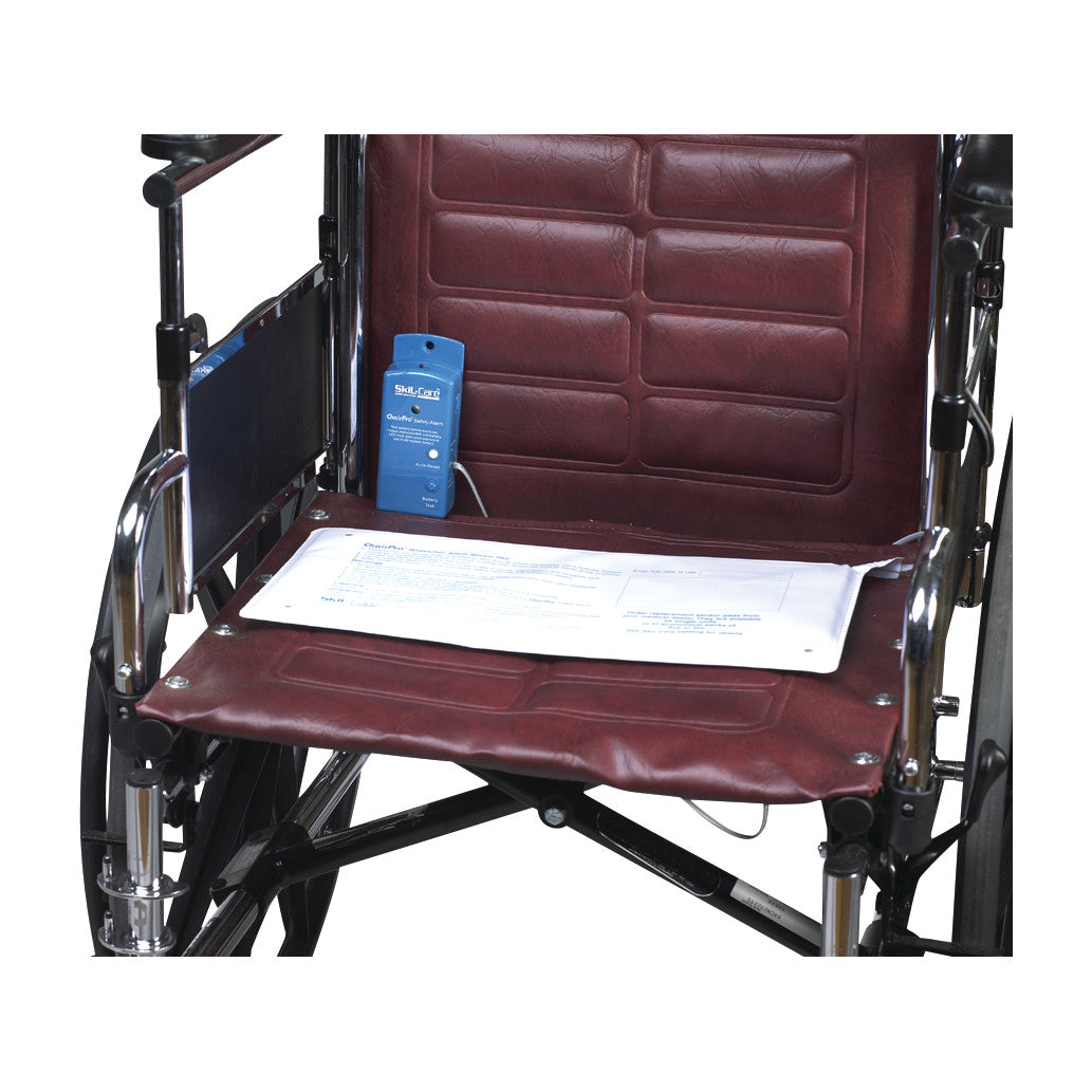 A SkiL-Care ChairPro Safety Alarm System is attached to a maroon wheelchair seat. A document rests on the seat.