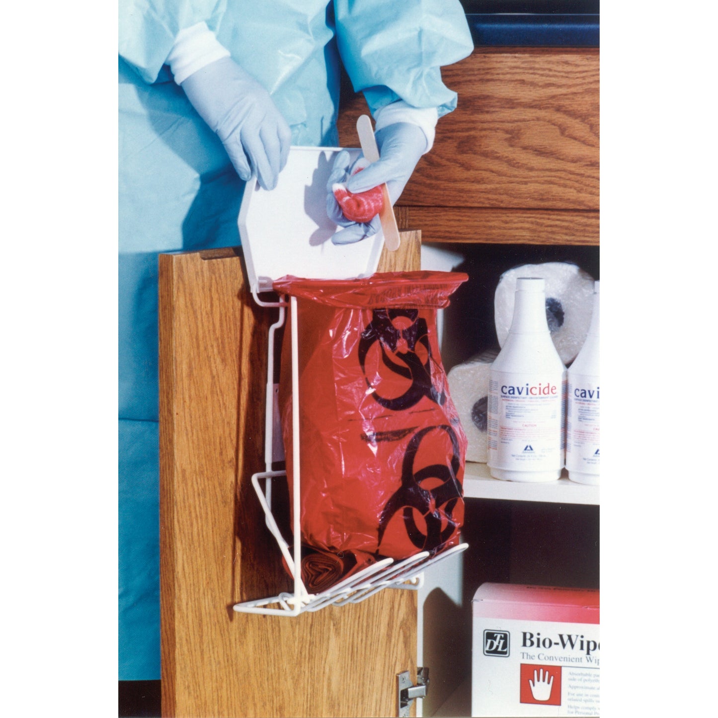 A Biohazard Waste Disposal Rack holds a red biohazard bag on a cabinet door. Nearby, cleaning supplies and Bio-Wipes are visible.