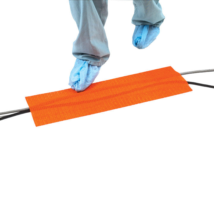 Person with shoe covers steps over SANDEL Trip-No-More Cord Alert, an orange mat covering cables to prevent tripping.