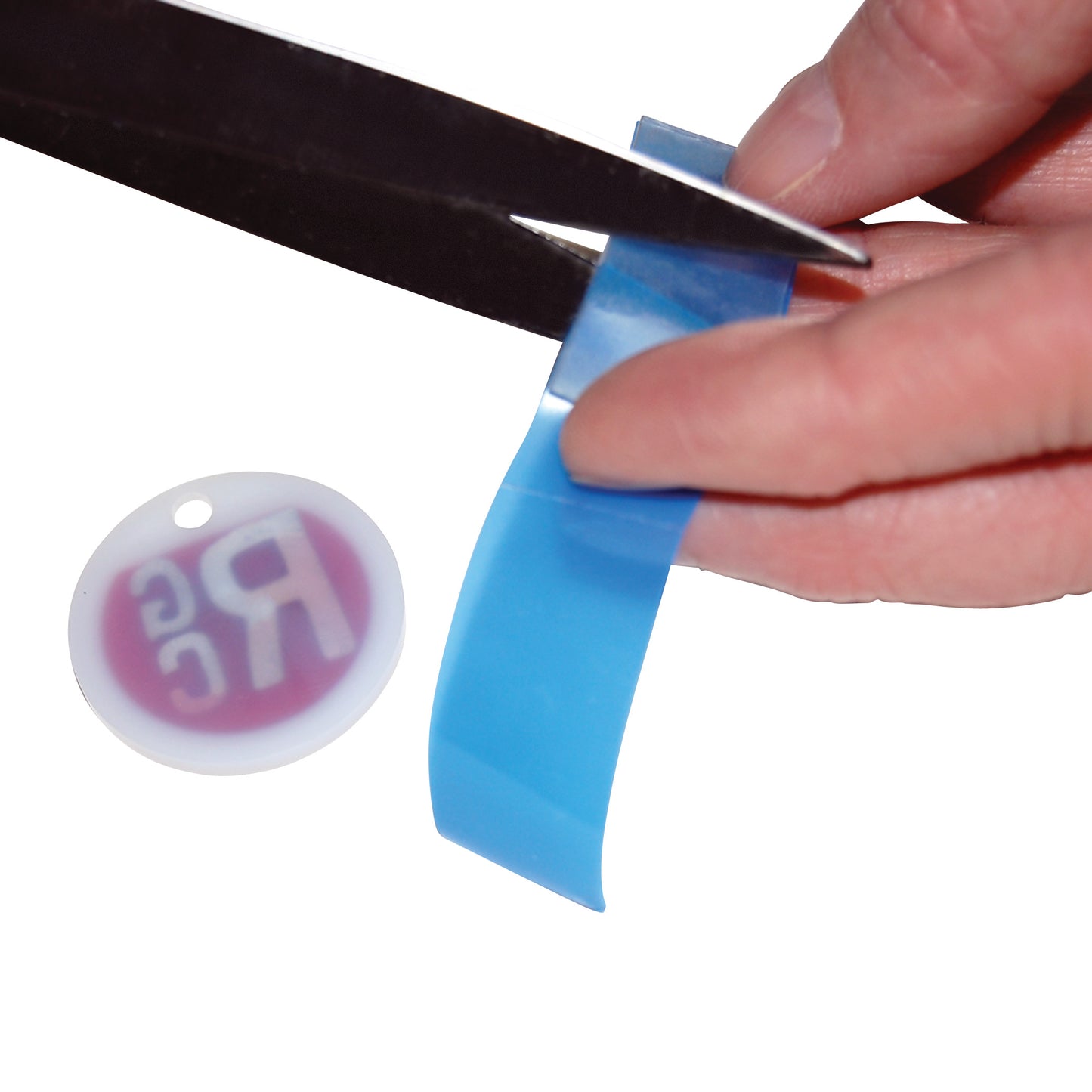 A hand cuts a blue strip of Marker Mate label tape with scissors. A round white tag with faint text is beside it.