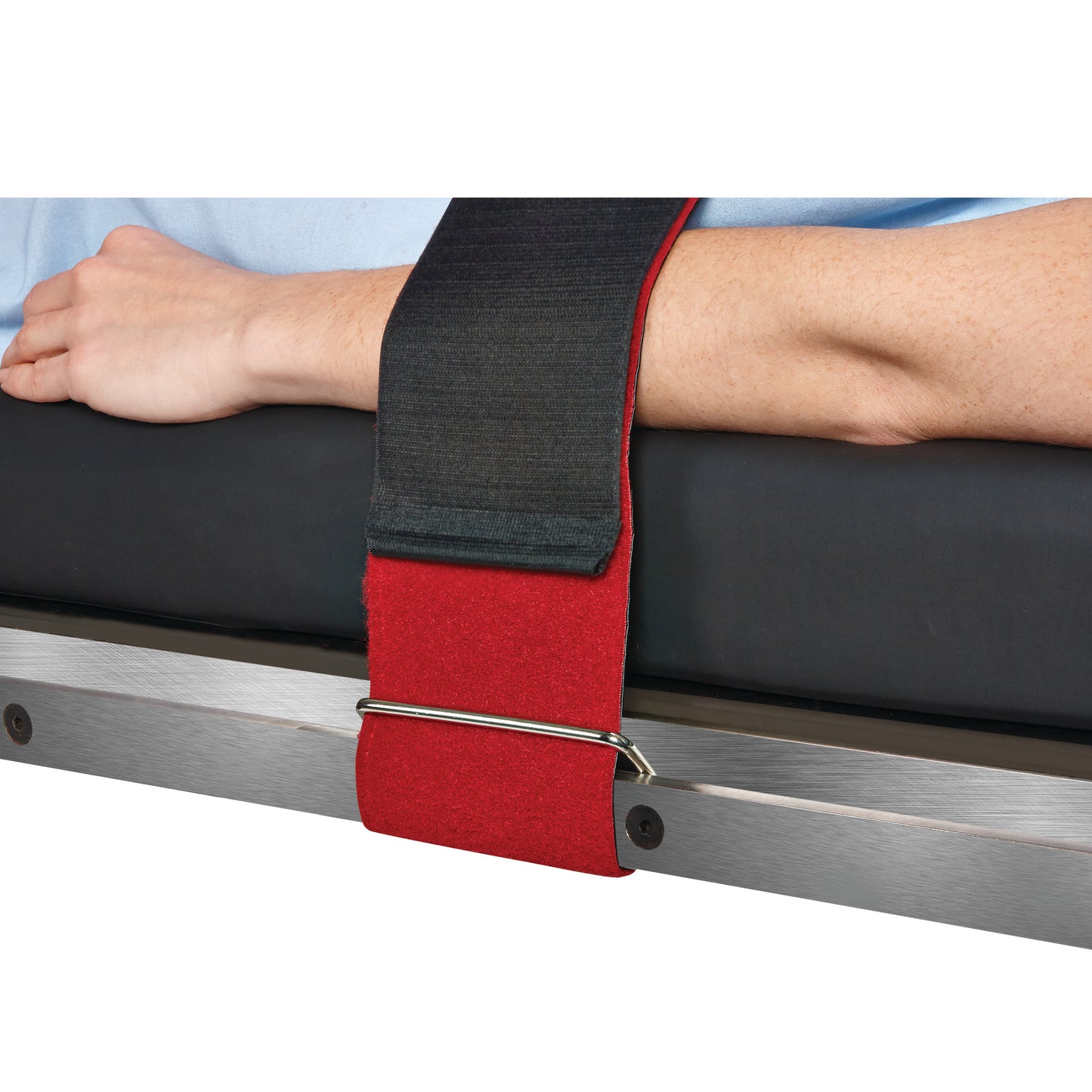 A person's arm is secured with a Covidien Devon Reusable Body/Knee Strap, featuring a red and black strap on a bed frame.