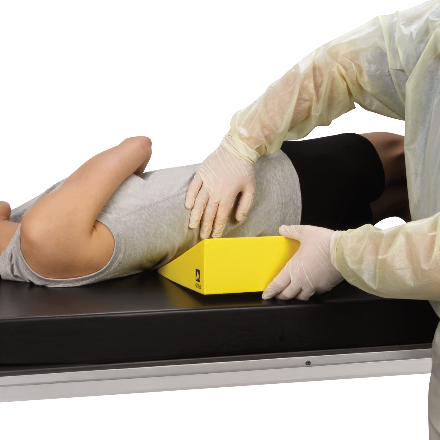 A healthcare worker positions a patient using an AliMed Protecta-Coat 20 Degree Wedge Positioner on an examination table.