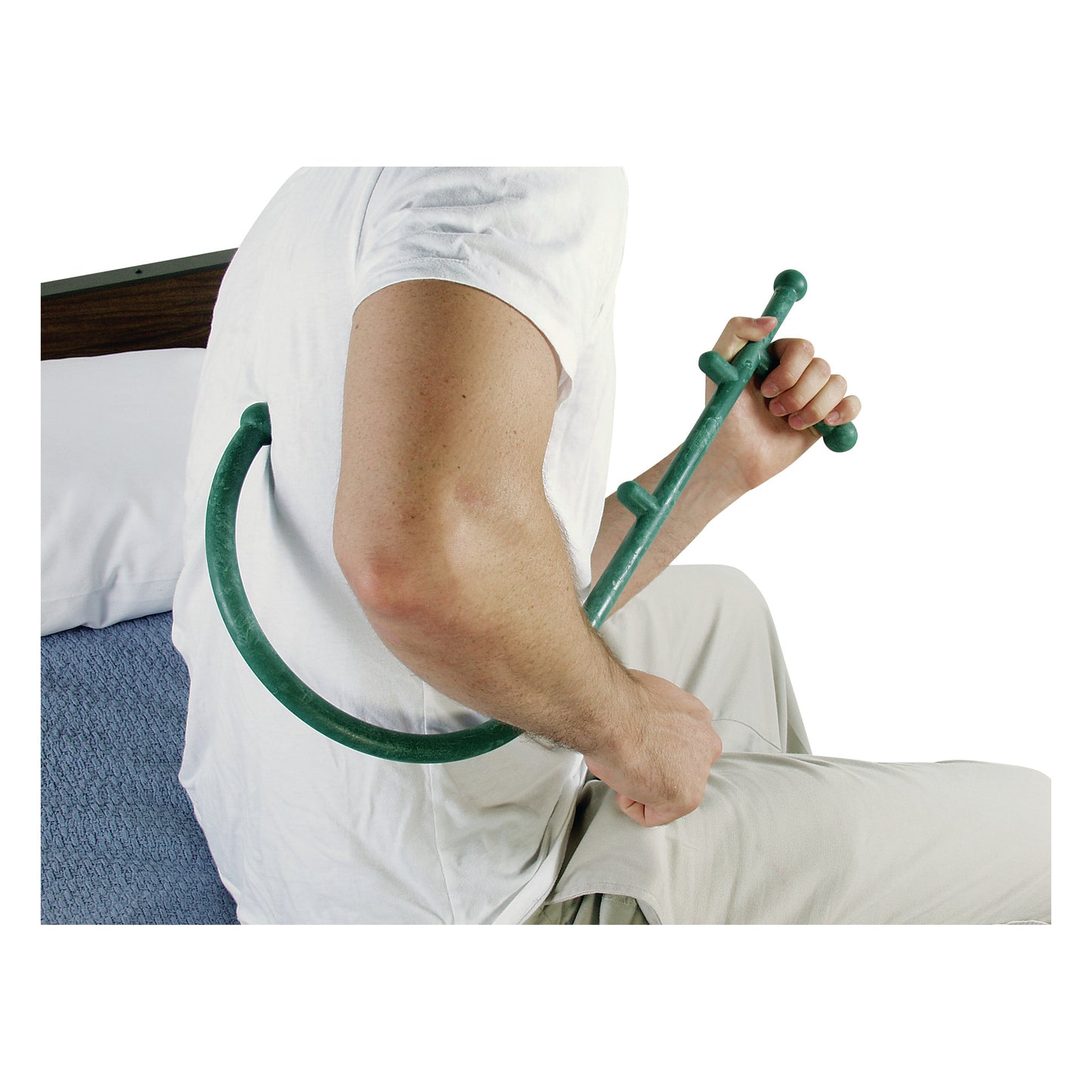 A person uses a Thera Cane Massager to apply pressure to their back muscle while sitting on the edge of a bed.