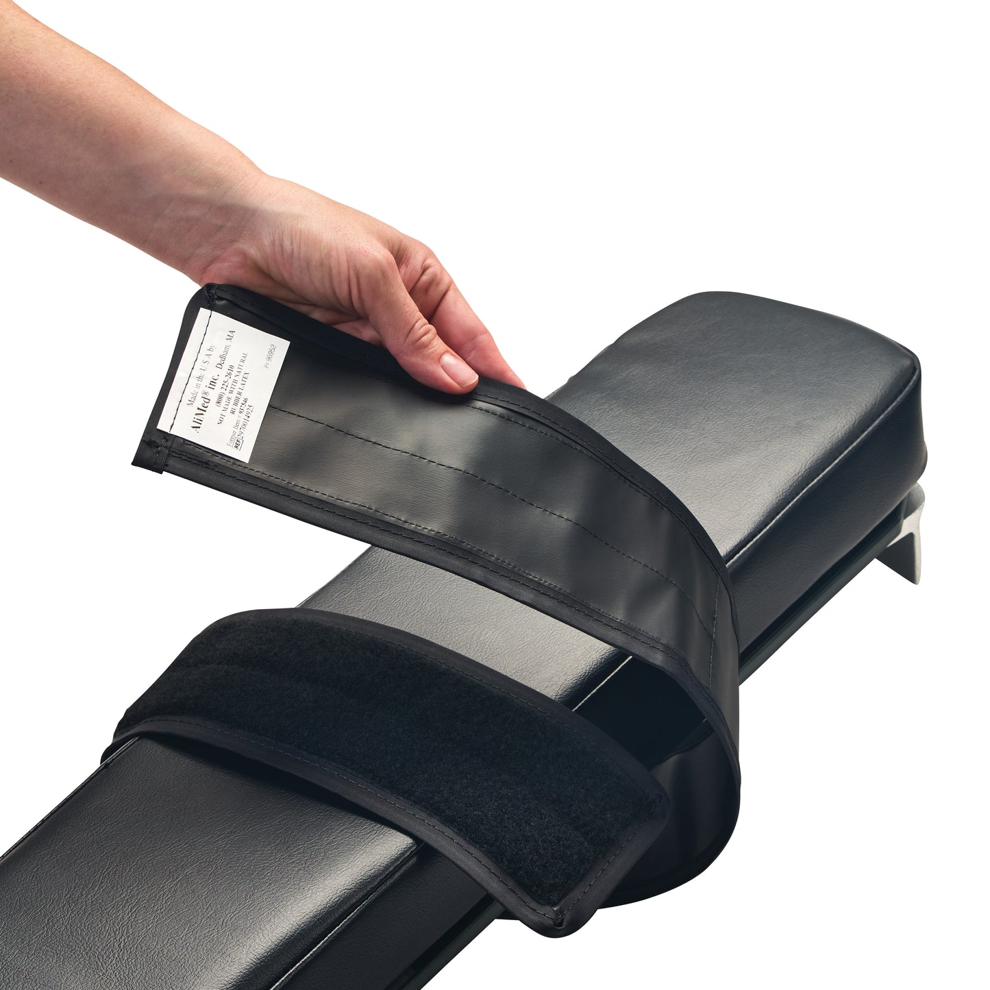 A hand holds the AliMed Reusable Armboard Strap over a black padded armboard, showing the adjustable Velcro strap design.