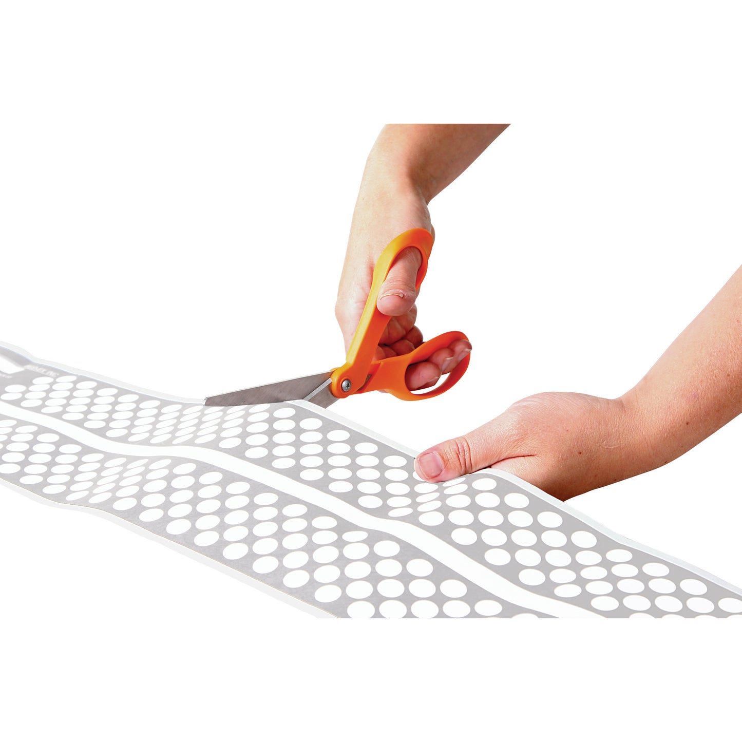 Hands cutting an AliMed Ultra-Thin Touch-Sensitive Sensor Pad with orange-handled scissors against a white background.