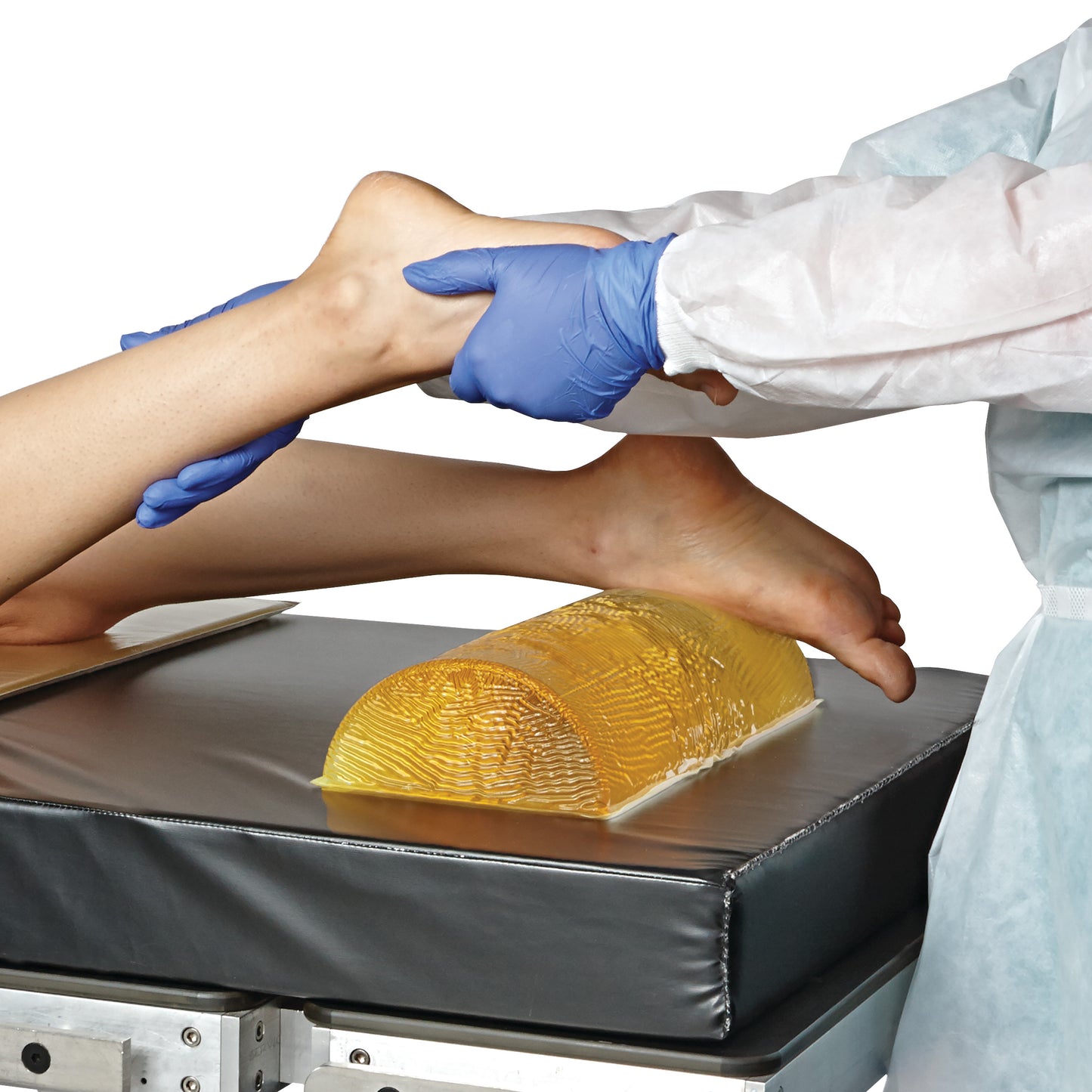 A person positions a leg using the AliMed AliGel Dome Positioner on a padded surface, wearing blue gloves and a protective gown.